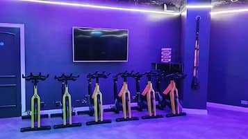 Une pièce aux murs violets, avec un téléviseur fixé au mur et une rangée de vélos d’appartement.