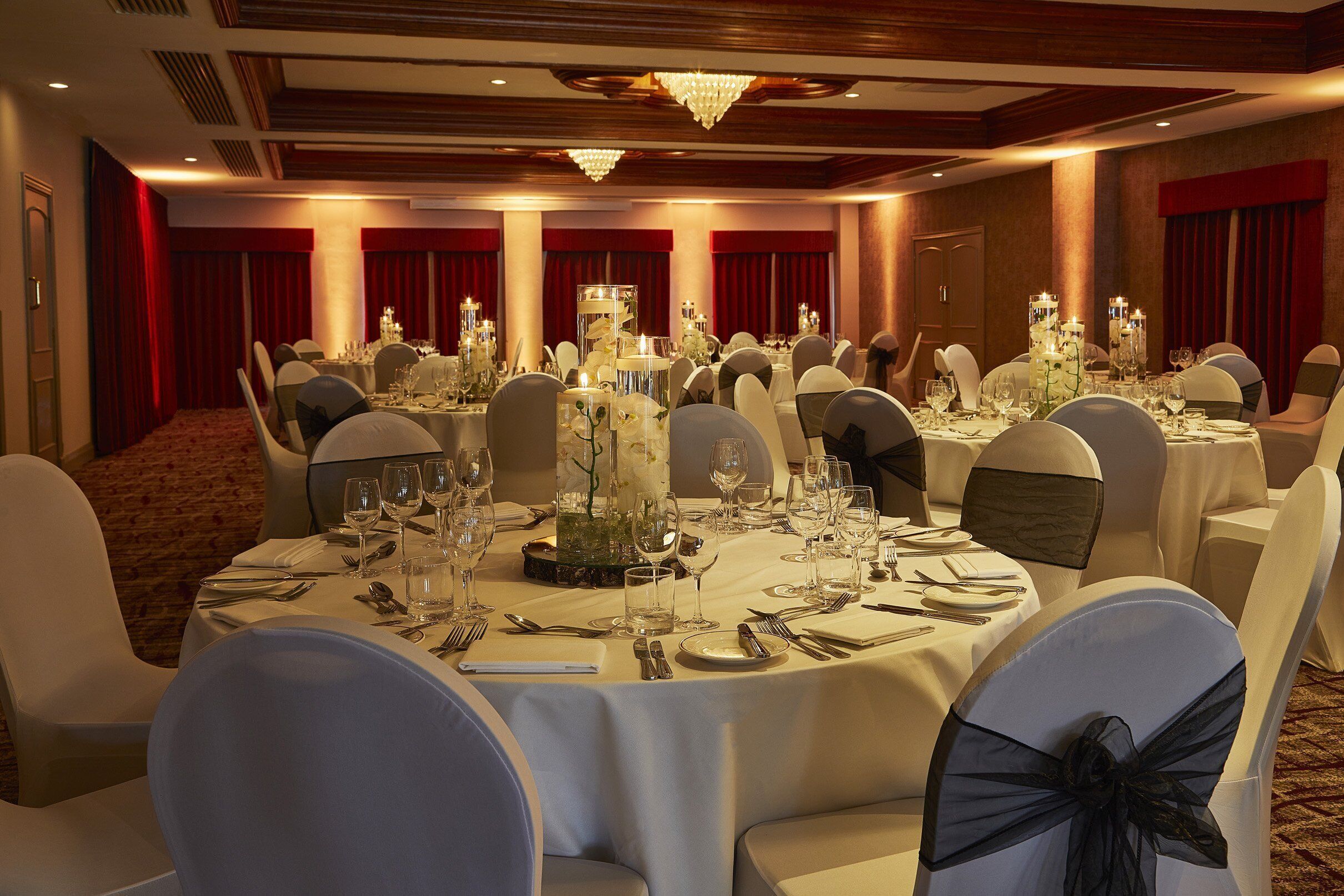 Un salón de banquetes con mesas redondas dispuestas para un evento formal, con candelabros y centros de mesa florales.