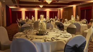 Un salón de banquetes con mesas redondas dispuestas para un evento formal, con candelabros y centros de mesa florales.