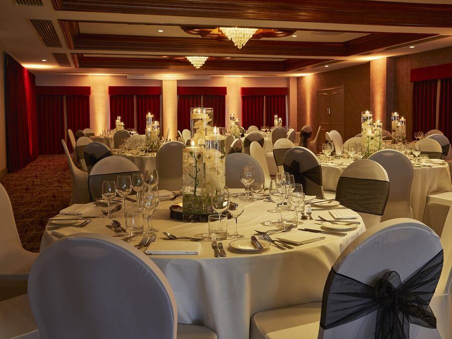 Un salón de banquetes con mesas redondas dispuestas para un evento formal, con candelabros y centros de mesa florales.