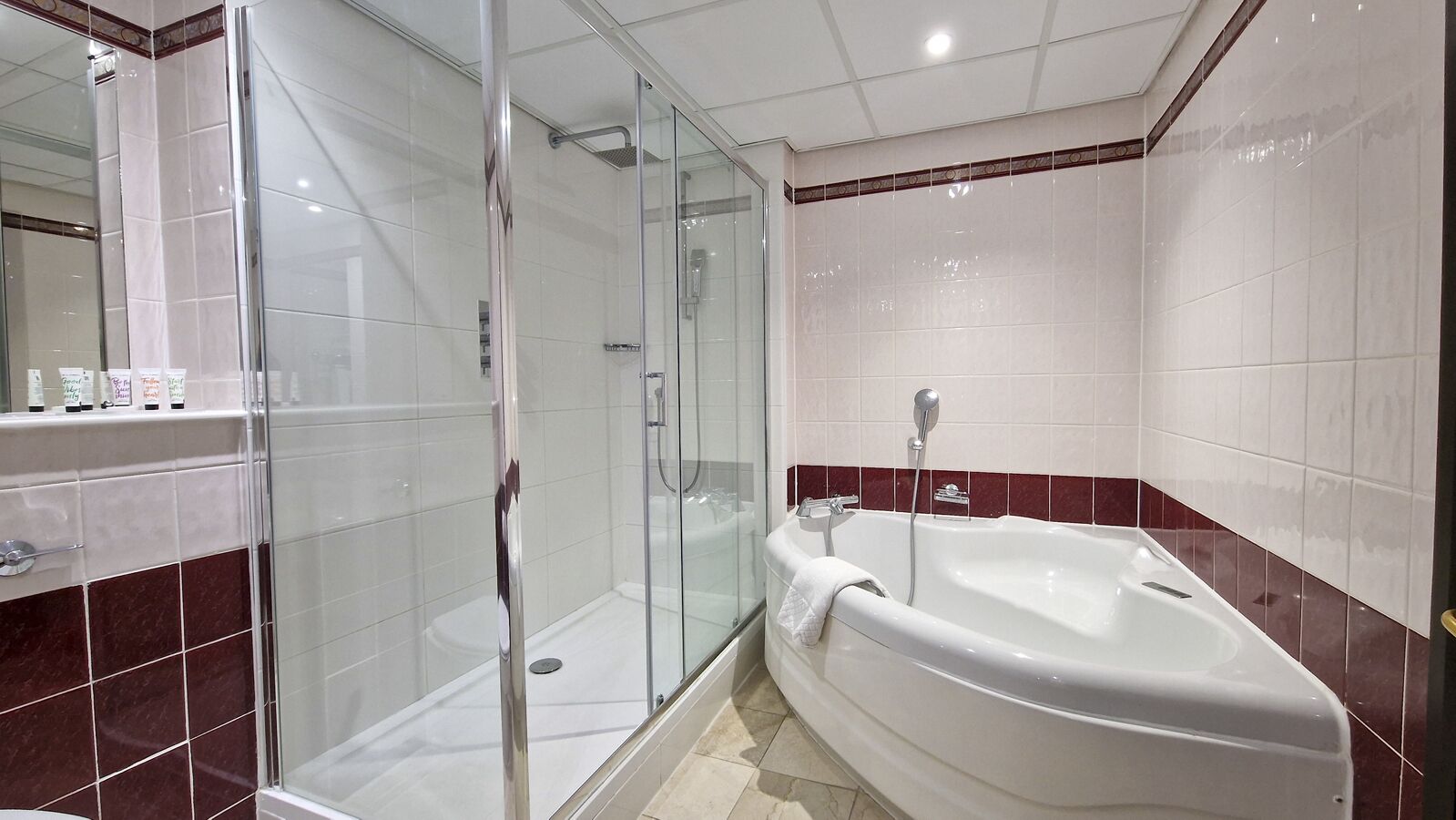 Un baño con ducha envuelta en vidrio, una bañera blanca y suelo de baldosas de mármol.