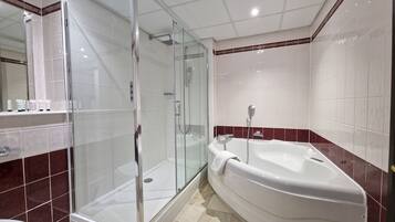 Un baño con ducha envuelta en vidrio, una bañera blanca y suelo de baldosas de mármol.