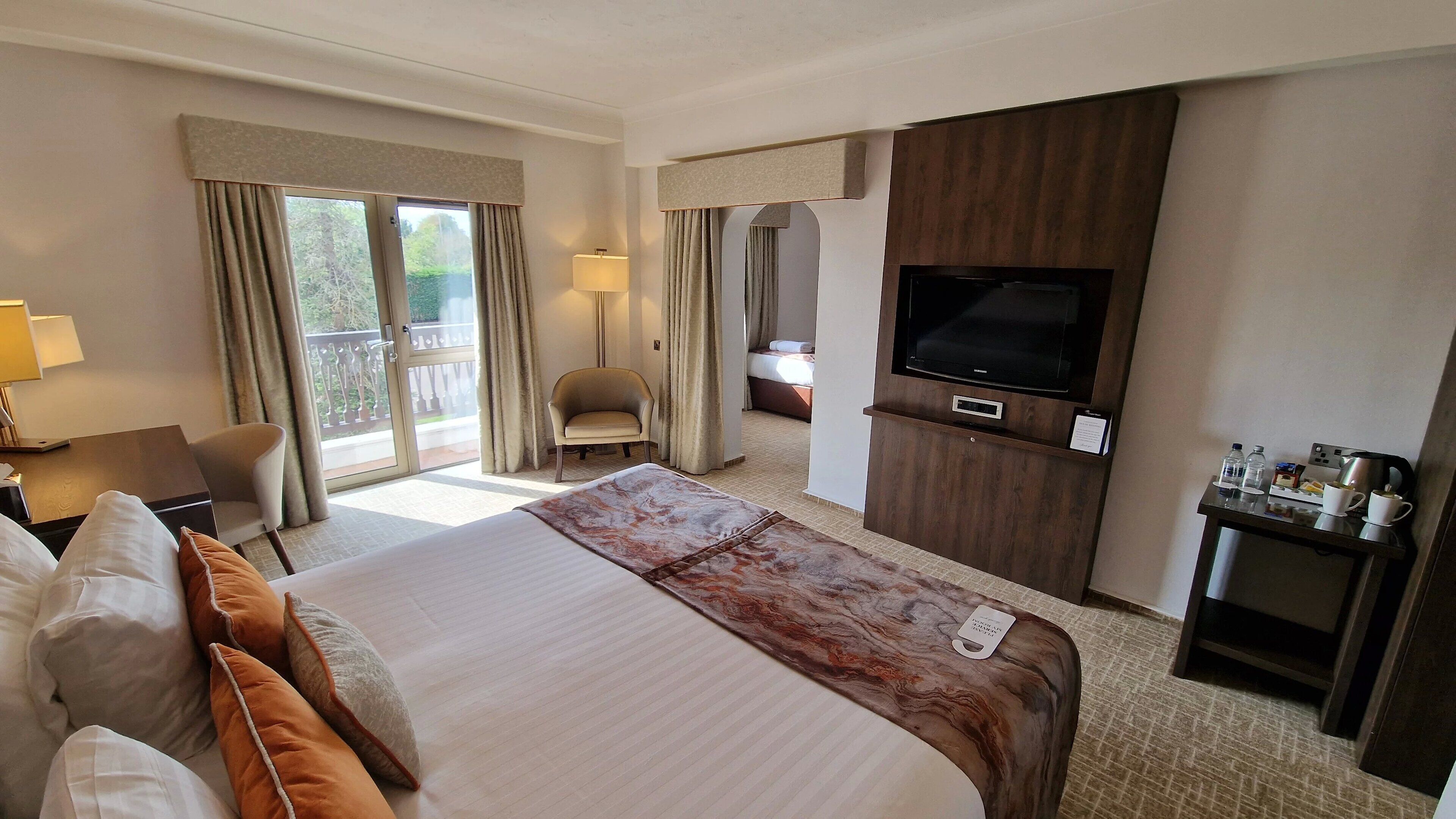 A hotel room with a large bed, a TV, a desk with a coffee maker, and a chair.