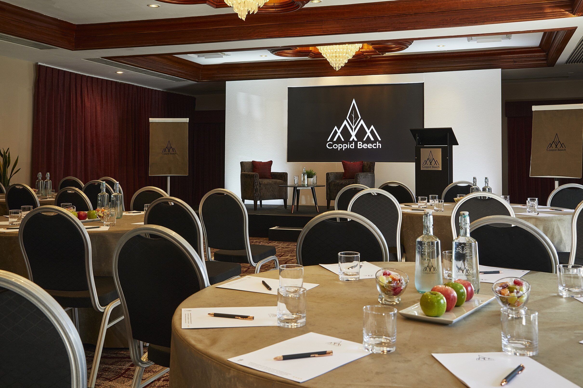 A conference room with round tables, chairs, and a stage with a presentation screen.
