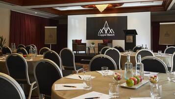 A conference room with round tables, chairs, and a stage with a presentation screen.