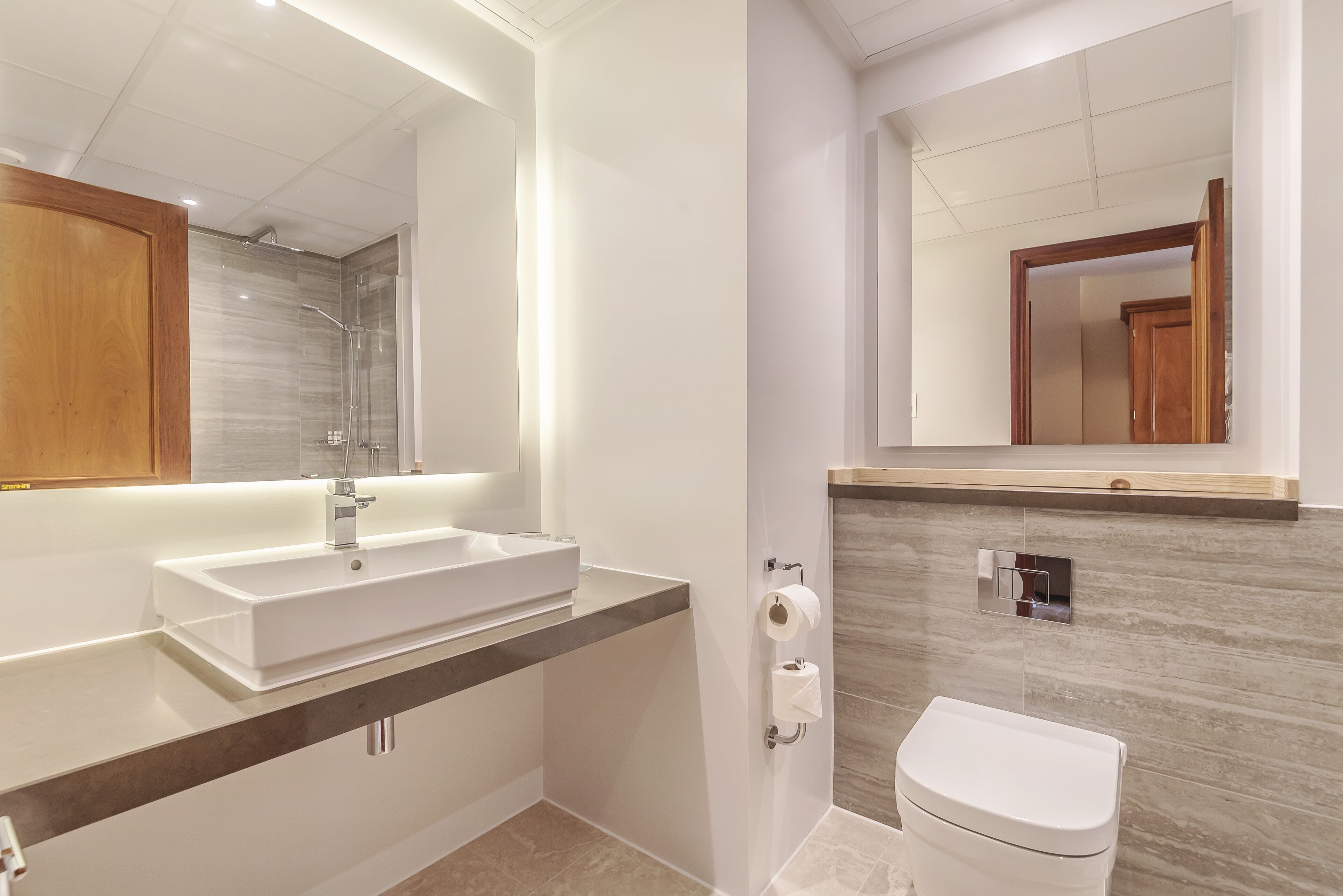 A modern bathroom with a large mirror, a white sink, and a toilet.