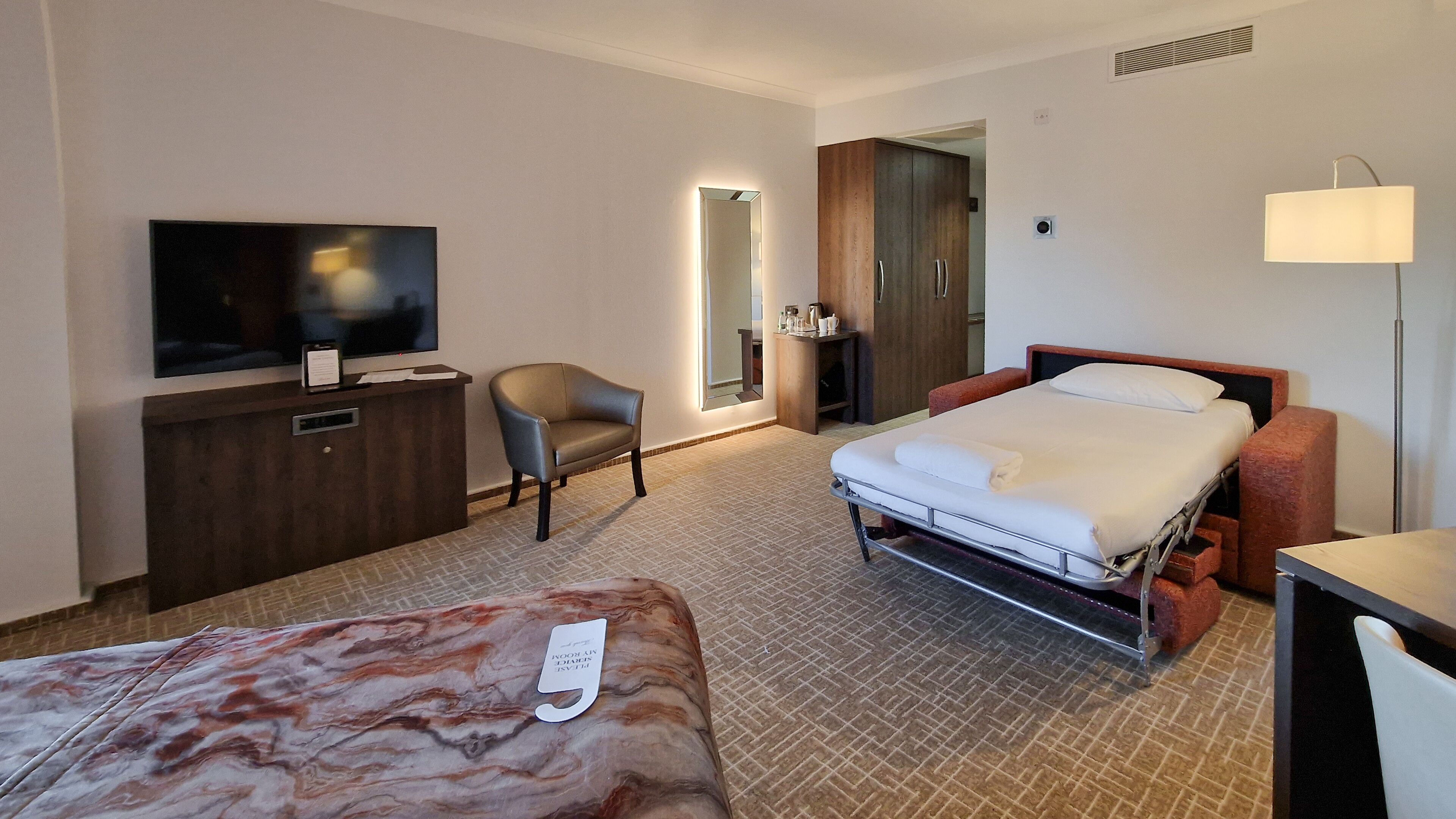 Ein Hotelzimmer mit Bett, Schreibtisch mit Fernseher, Stuhl, Kleiderschrank und Nachttisch.