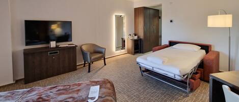 Ein Hotelzimmer mit Bett, Schreibtisch mit Fernseher, Stuhl, Kleiderschrank und Nachttisch.