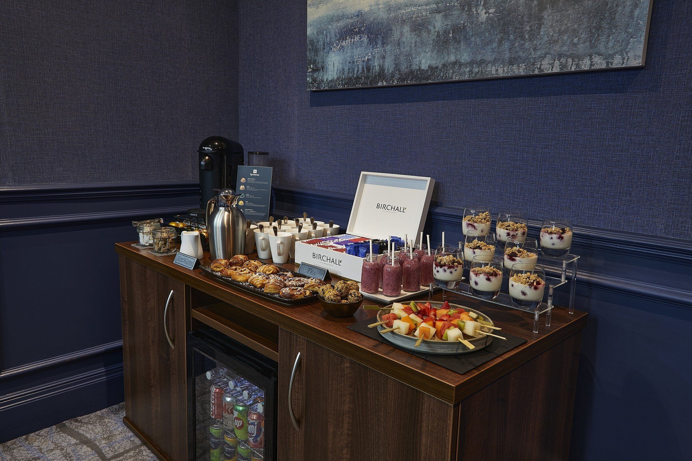 A buffet setup with various food items, a coffee machine, and a beverage cooler.