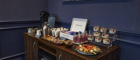 A buffet setup with various food items, a coffee machine, and a beverage cooler.