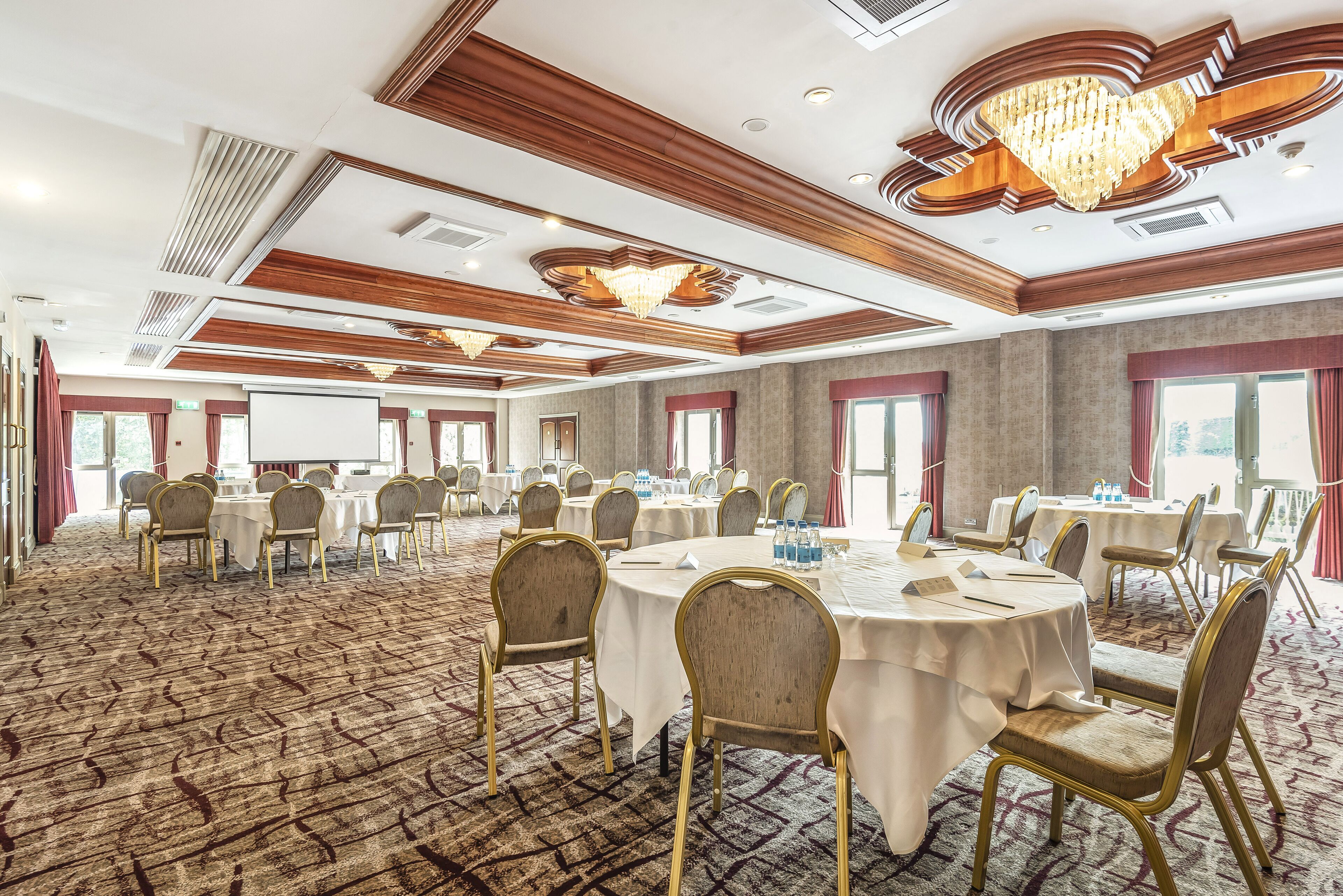 A large conference room with round tables and chairs, a patterned carpet, and a chandelier.