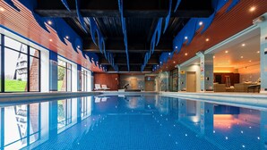 An indoor swimming pool with clear blue tiles, wooden ceiling beams, and a view of the outside. - The Coppid Beech Hotel (Bracknell)