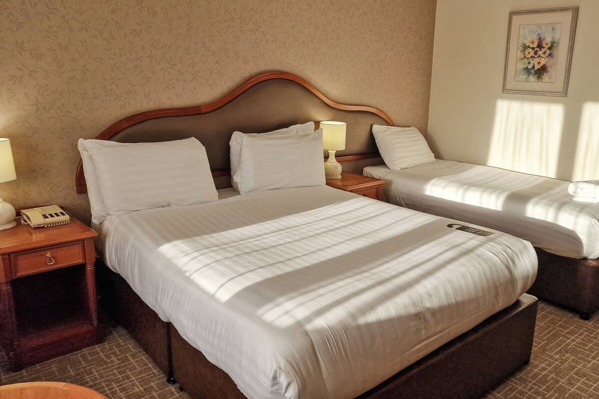 A hotel room with two beds, a wooden headboard, bedside tables with lamps, a telephone, and a framed picture on the wall.
