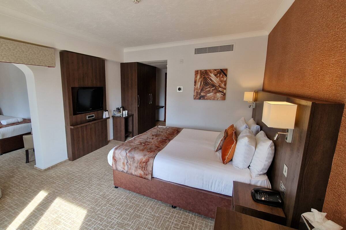 A hotel room with a large bed, a TV, a desk with a phone, and a bathroom visible through an open door.