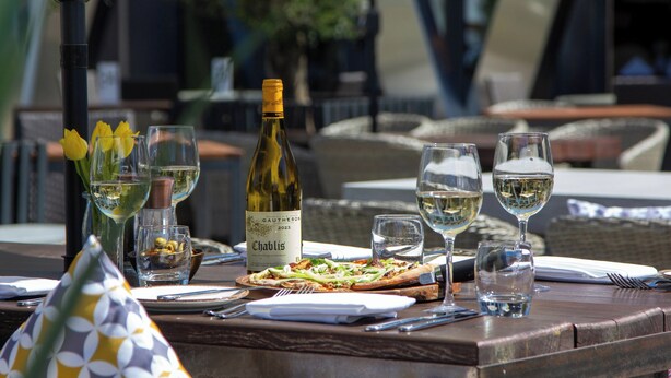 A dining table set with a bottle of wine, glasses, a plate of food, and a vase with flowers. - The Coppid Beech Hotel (Bracknell)