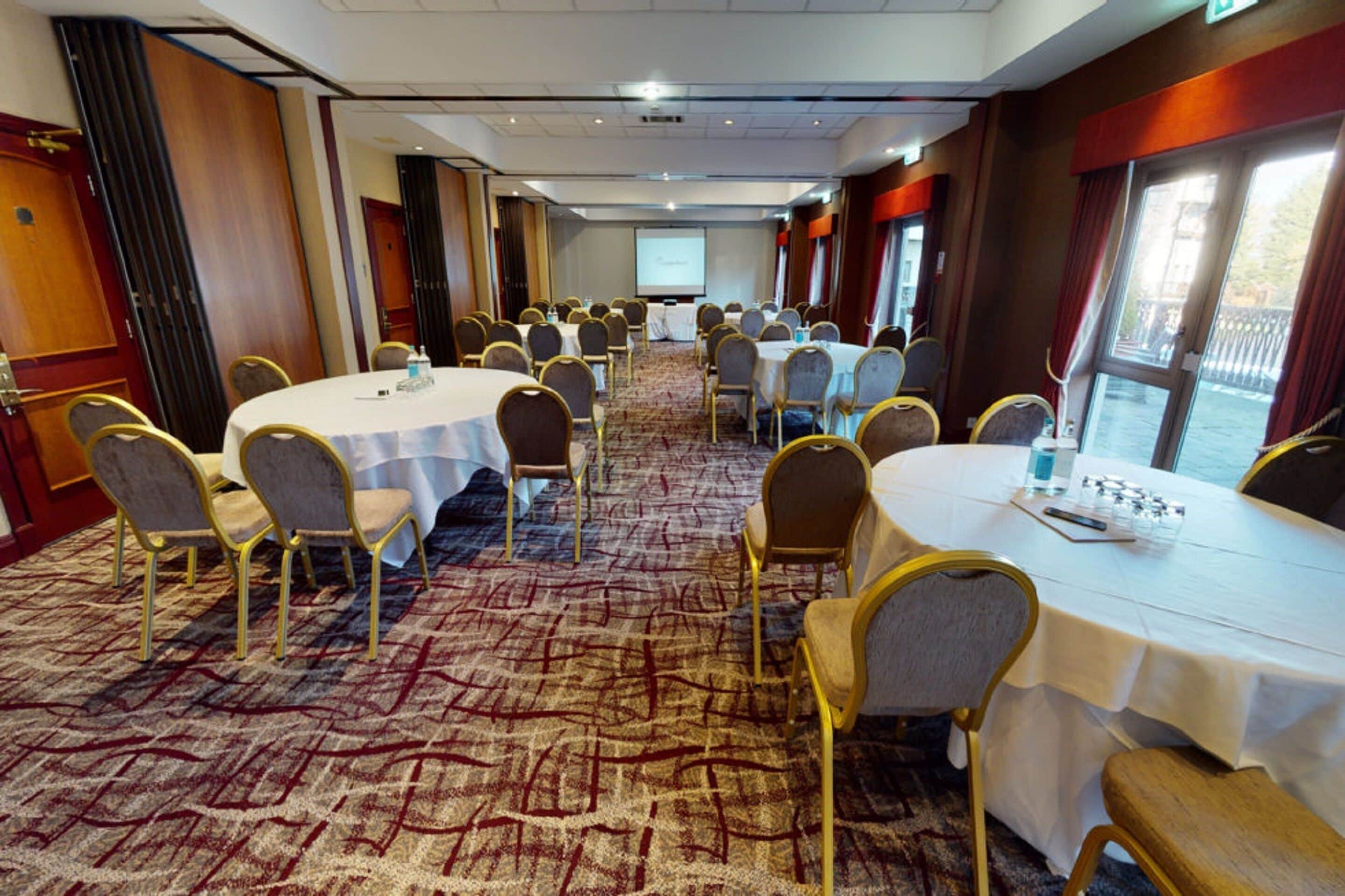 A conference room with round tables, chairs, and a carpeted floor.