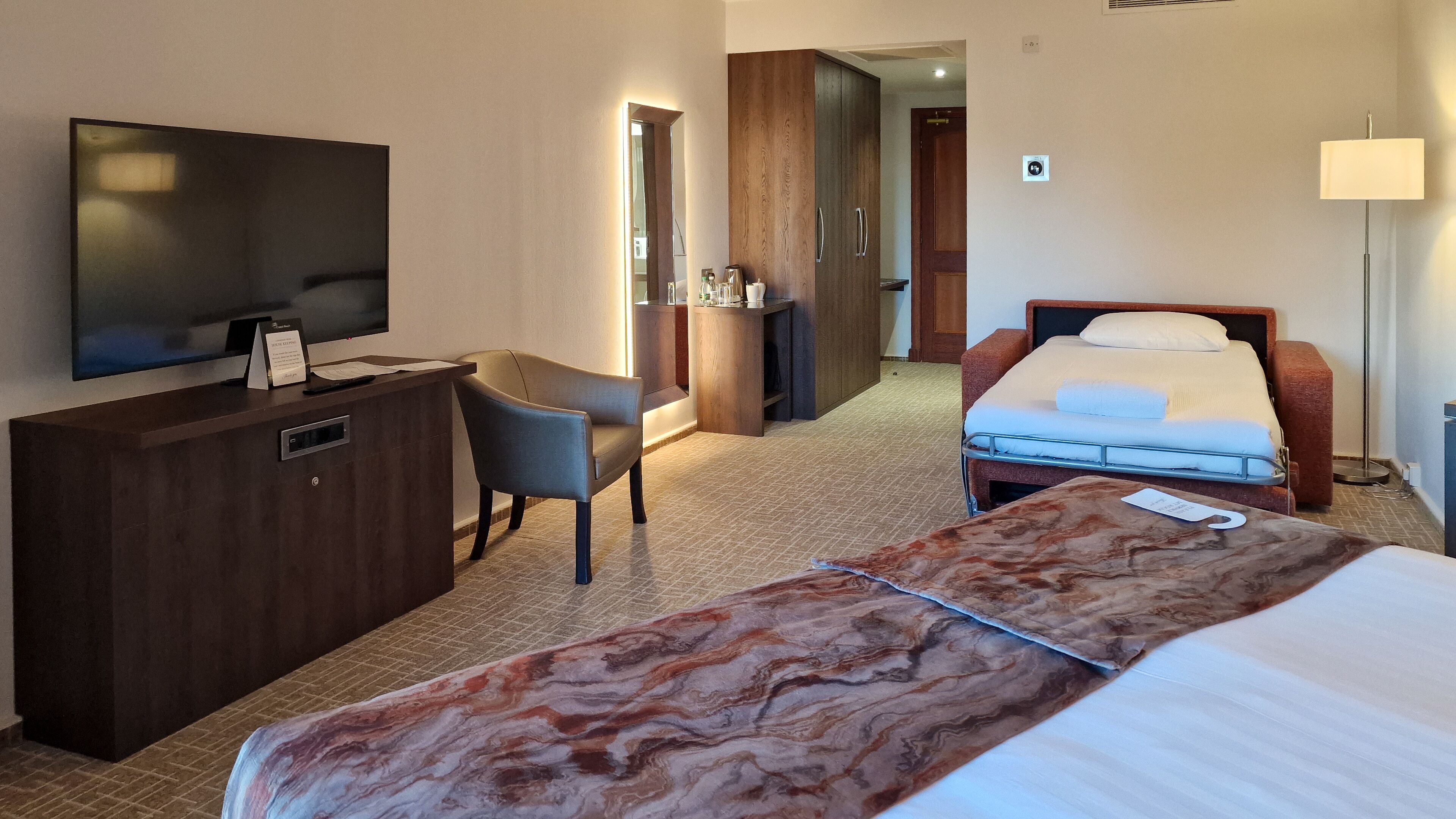 Een hotelkamer met een bed, een bureau met een televisie, een stoel en een nachtkastje.