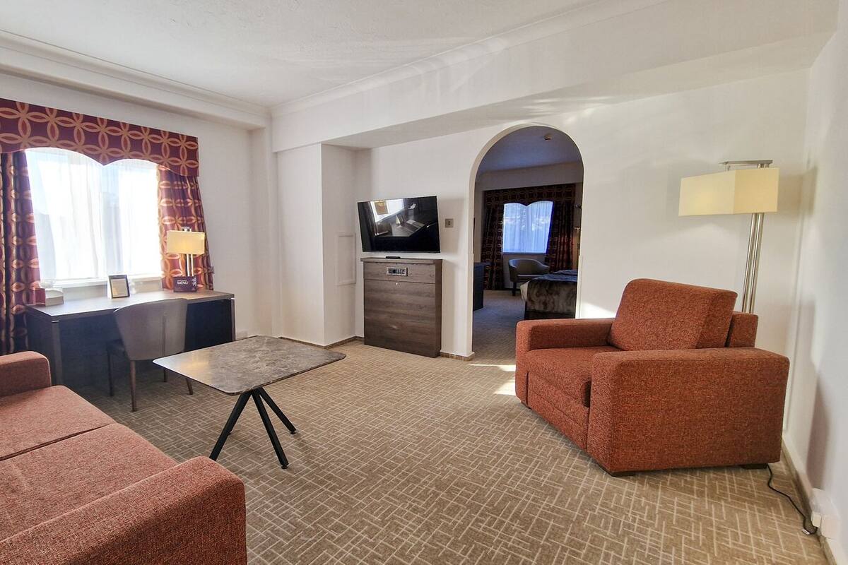 A hotel room with a sofa, a small table, a TV, a desk, and a lamp.