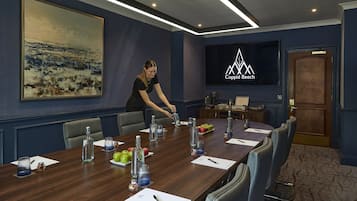 Un salón de conferencias con una mesa larga, sillas, una pantalla de televisión y un cuadro en la pared.