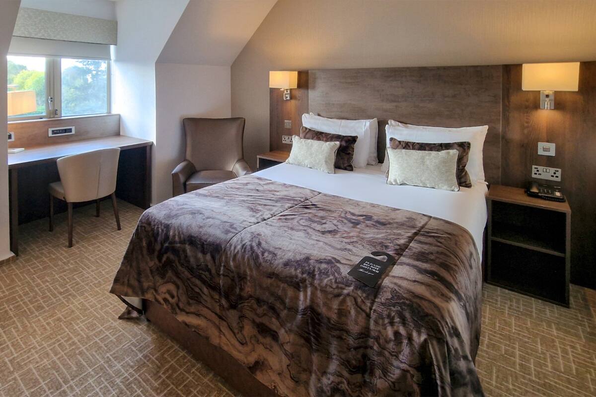 A hotel room with a large bed, a desk, a chair, and a TV.