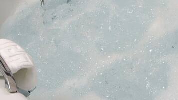 A bathtub filled with water and bubbles, a white towel, and a metal faucet.