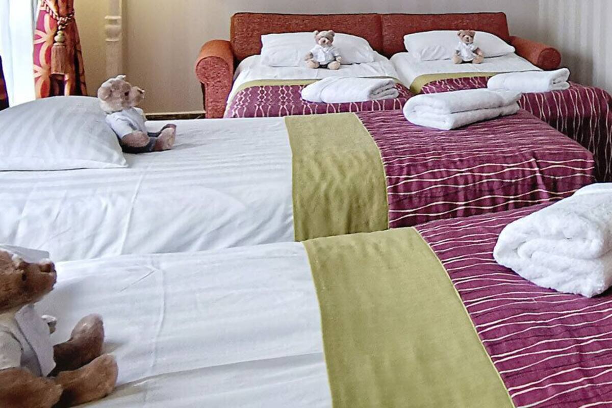 A hotel room with two beds, each with a teddy bear, a chair, a table, and a lamp.