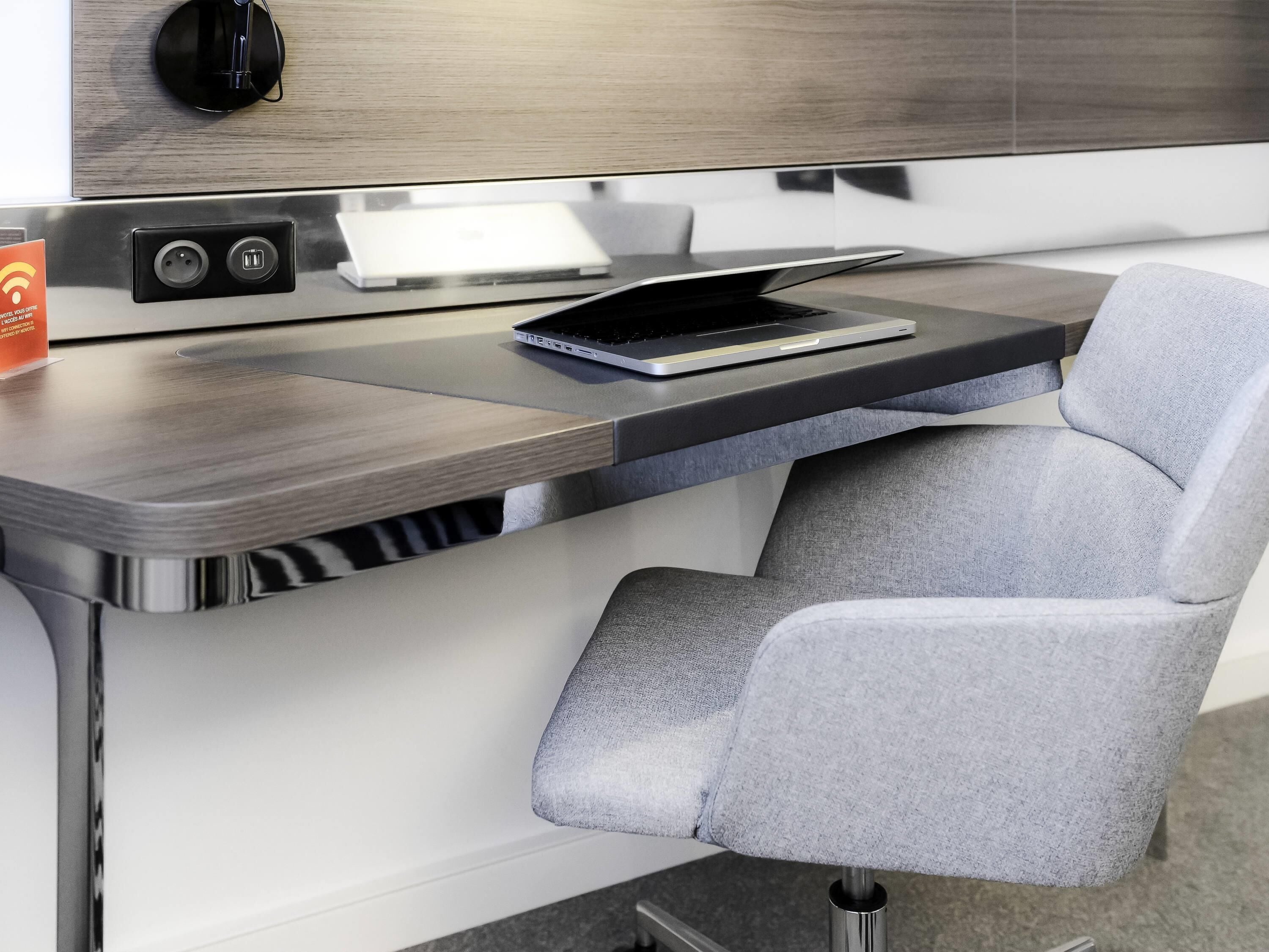 A modern hotel desk with a laptop, power outlets, and a charging station.