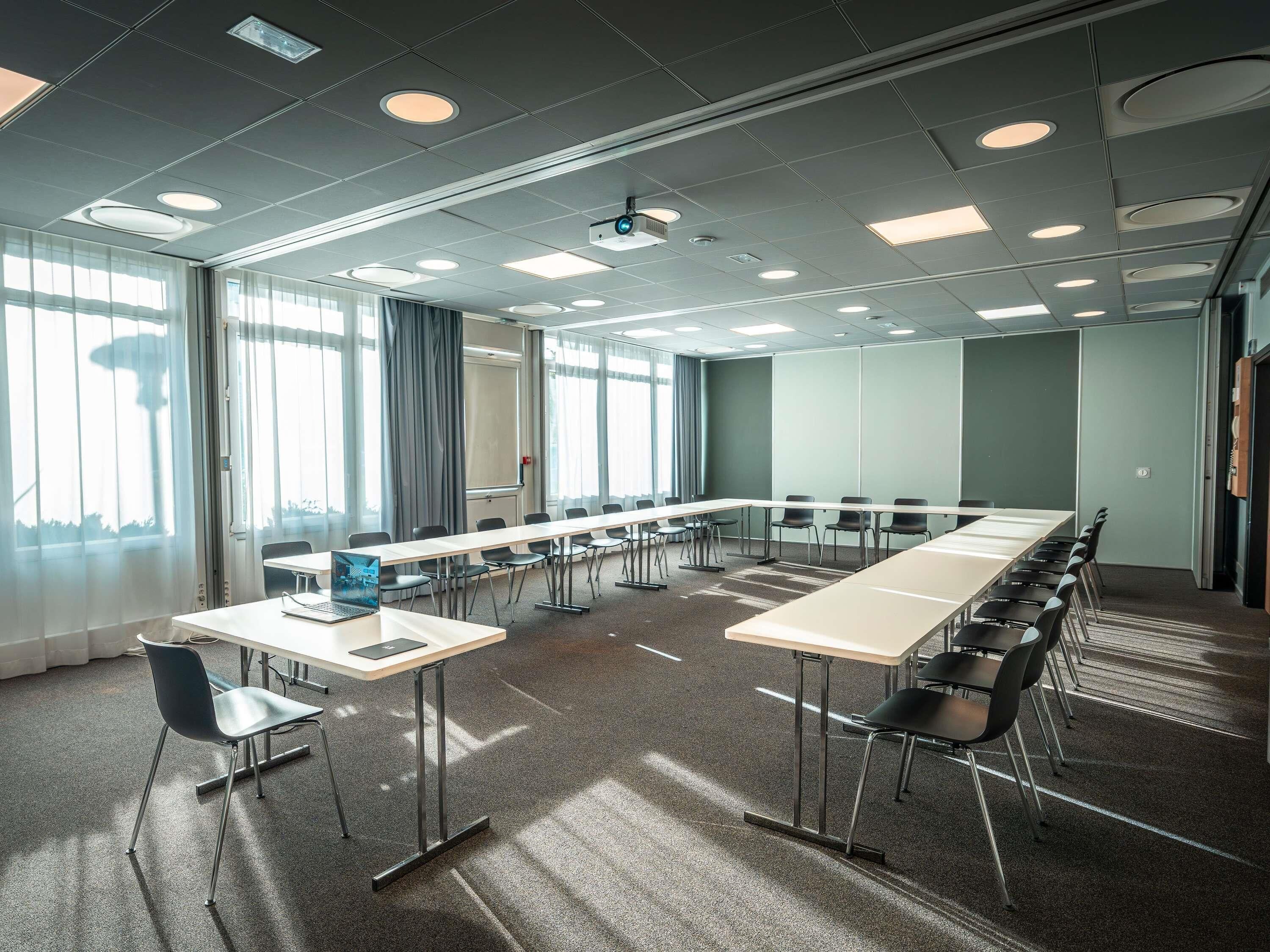 A conference room with a long table, chairs, a projector, and a large window.