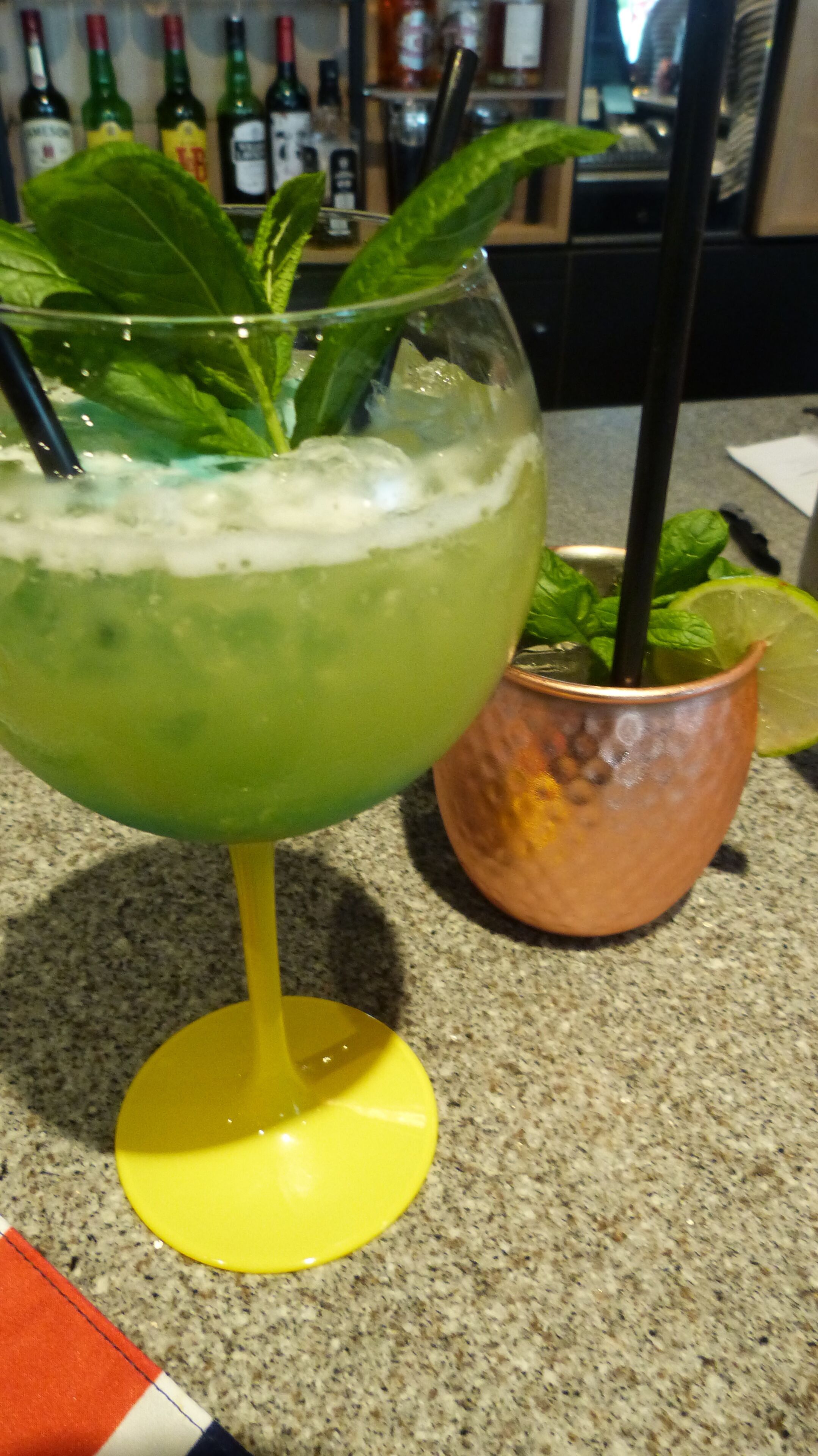 A cocktail glass with a lime wedge and mint leaves on a granite countertop.