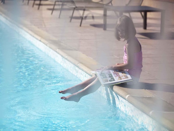A person sitting by a pool with a magazine.