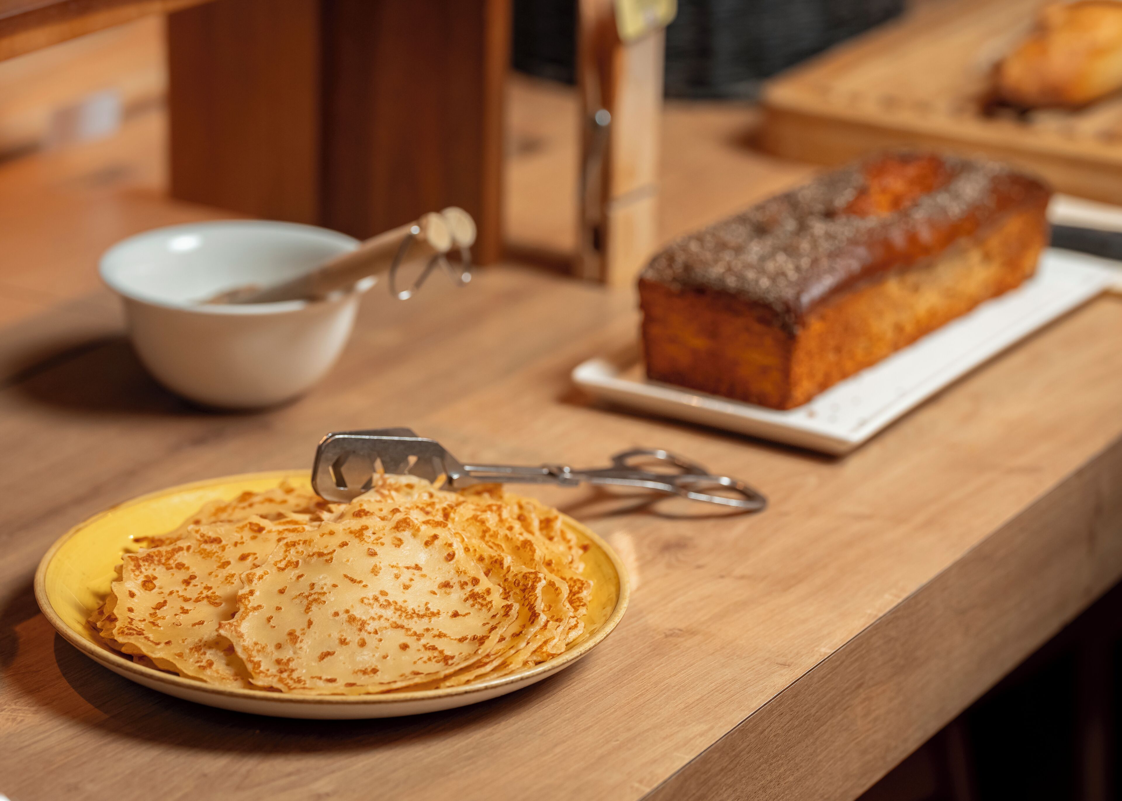 Una mesa de madera con una fuente de crepas y una hogaza de pan.