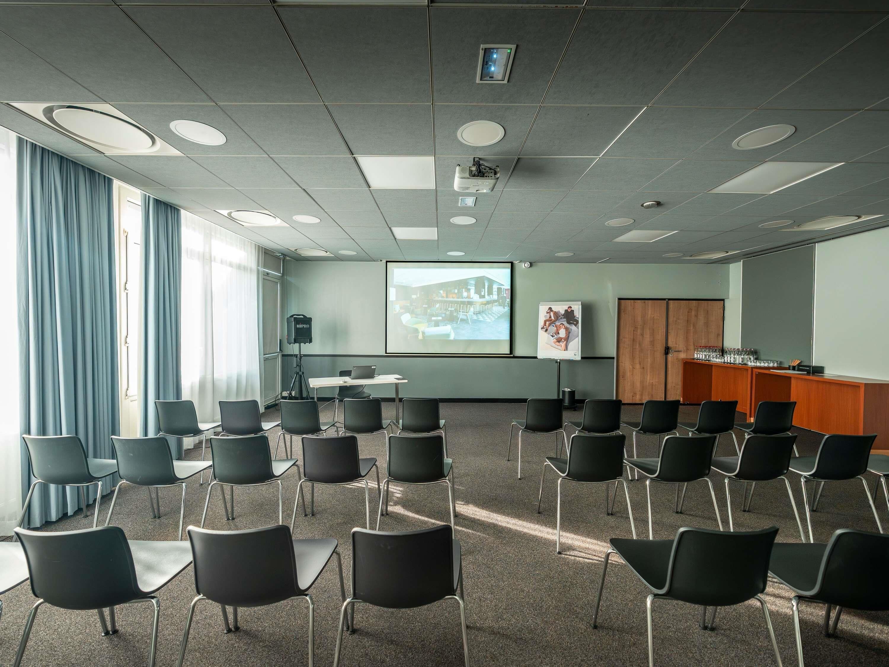 Uma sala de conferência com tela de projetor, quadro branco e um armário de madeira.
