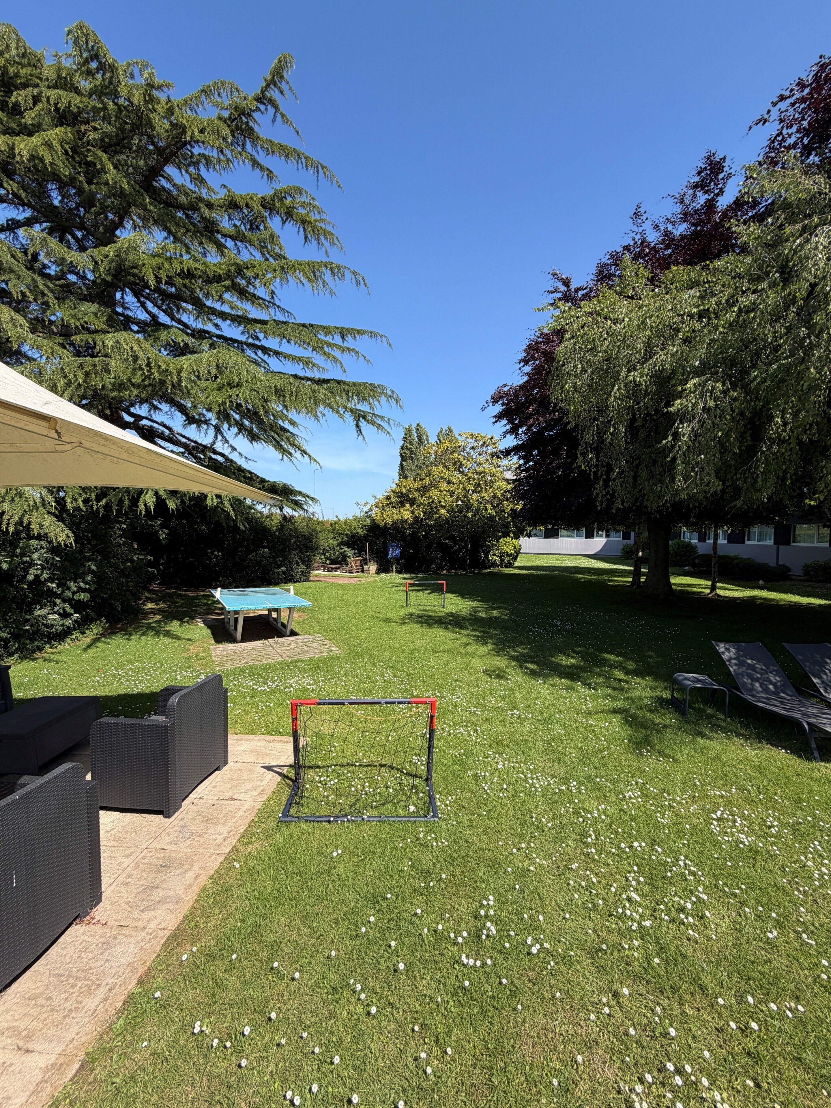 A grassy outdoor area with a patio, a table, and a goalpost.