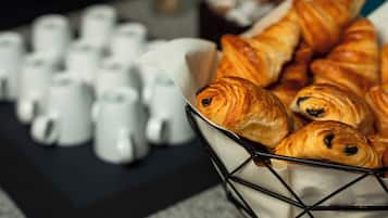A basket of croissants and a row of white ceramic cups on a table.