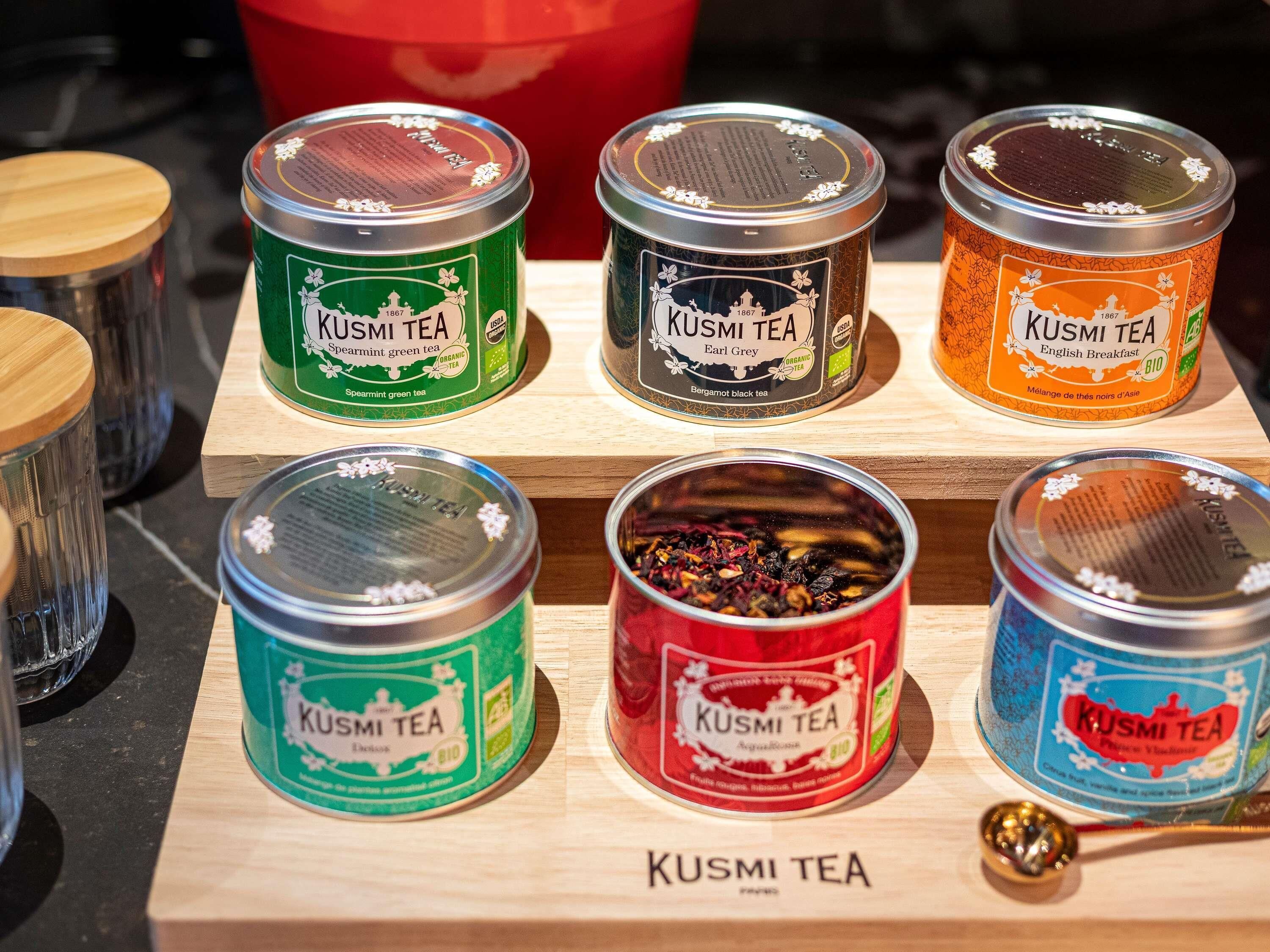 A display of various KUSMI TEA tins on a wooden shelf.