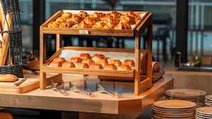 Una vitrina de madera con pasteles y croissants, junto con un cuchillo y tabla de cortar, y una cesta de mimbre con baguettes.