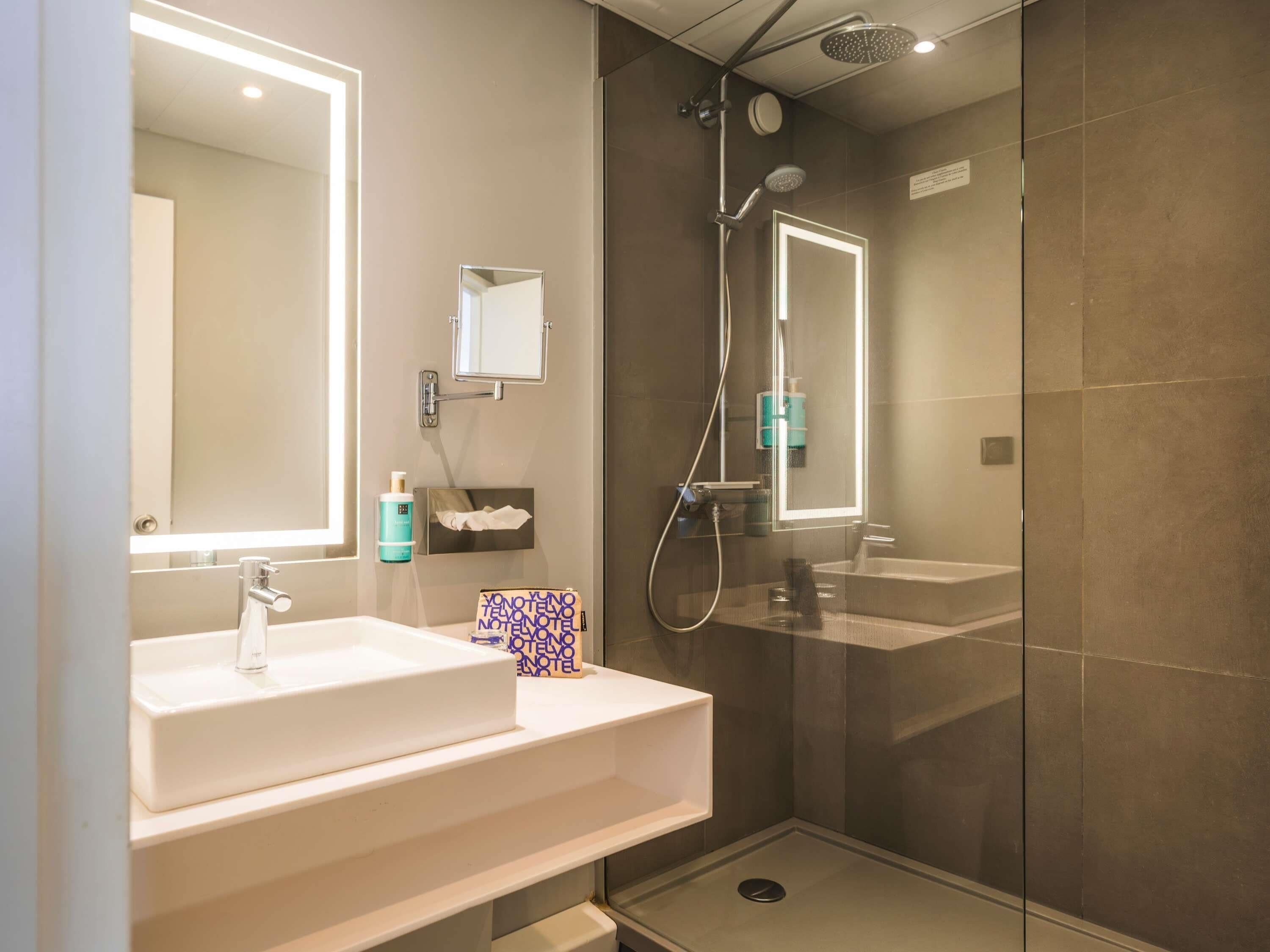 Un baño moderno con un espejo grande, un lavamanos, una ducha y zona de ducha con mampara de vidrio.