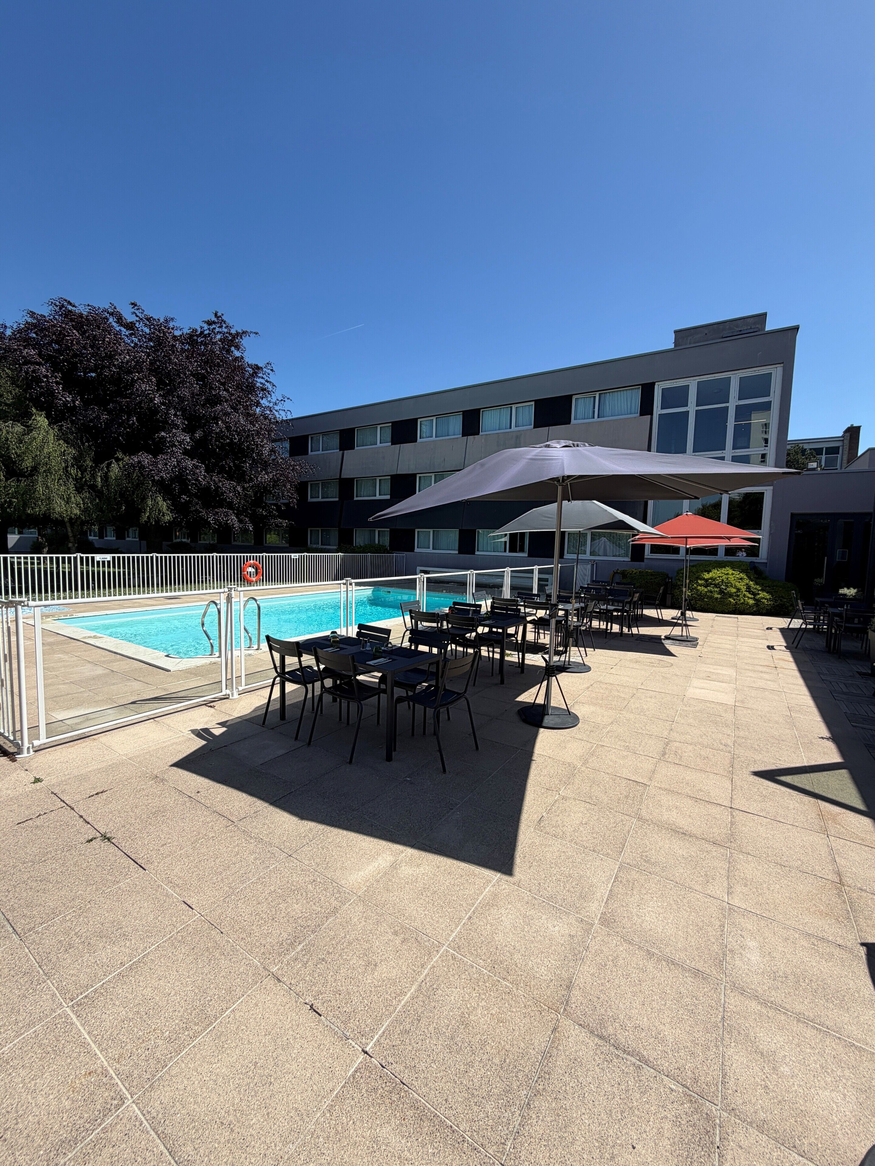 Et tagområde med swimmingpool, udendørs siddepladser og en bygning i baggrunden.