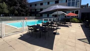 Et tagområde med swimmingpool, udendørs siddepladser og en bygning i baggrunden.