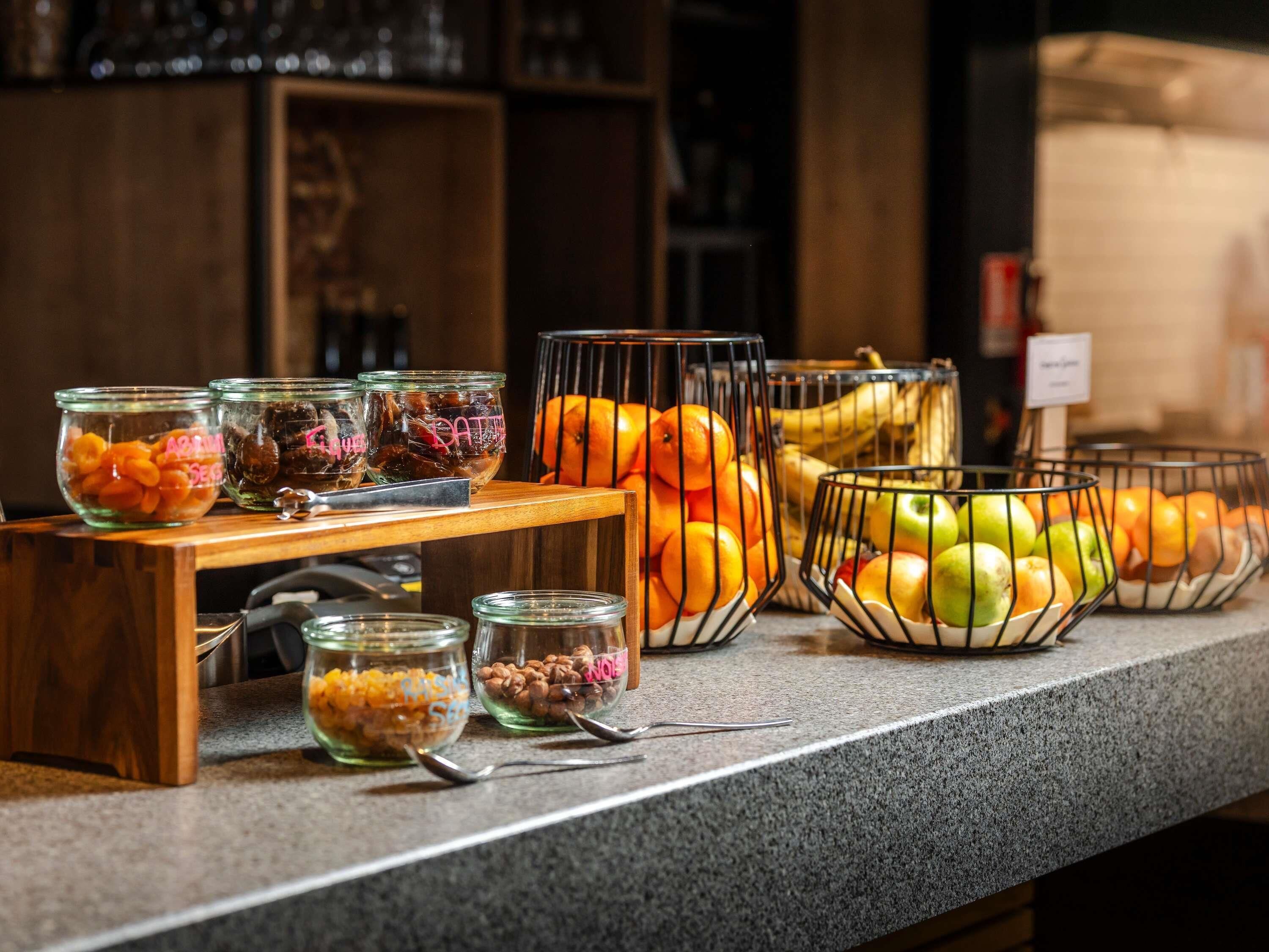 A buffet counter with various food items in glass containers and wire baskets, including fruits and nuts.