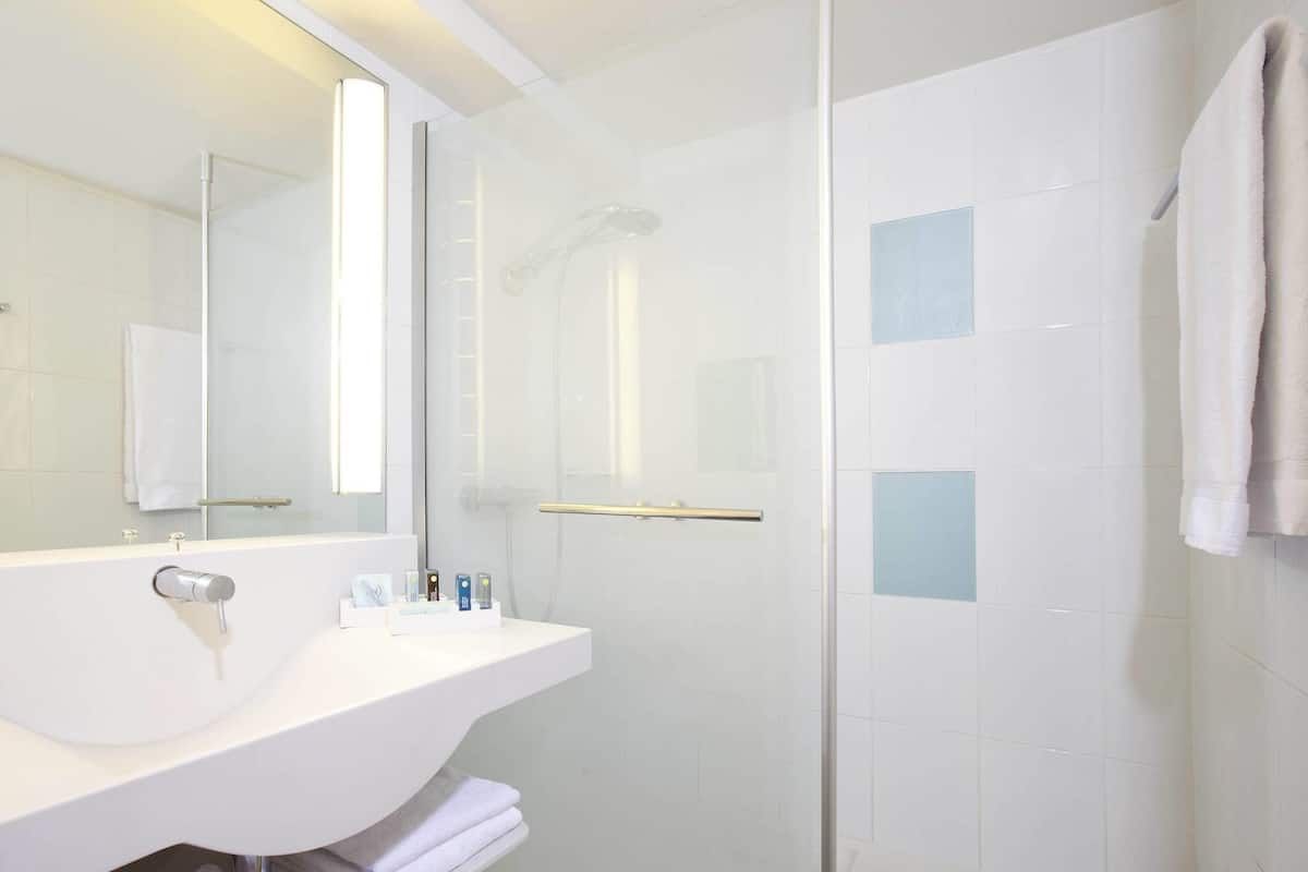 Un baño moderno con cabina de ducha de vidrio, lavamanos blanco y espejo.