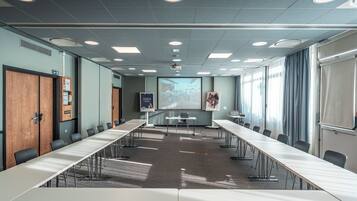 A conference room with a long table, chairs, a projector screen, and a presentation wall.
