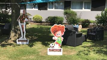 A grassy outdoor area with a sign for Hotel Transylvanie 3, a statue, and outdoor furniture.