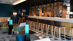 Zona de bar con taburetes, una barra y estantes con botellas.
