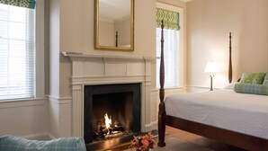 A bedroom with a fireplace, a bed, a nightstand, and a window with a view. - Kings Courtyard Inn (Charleston)