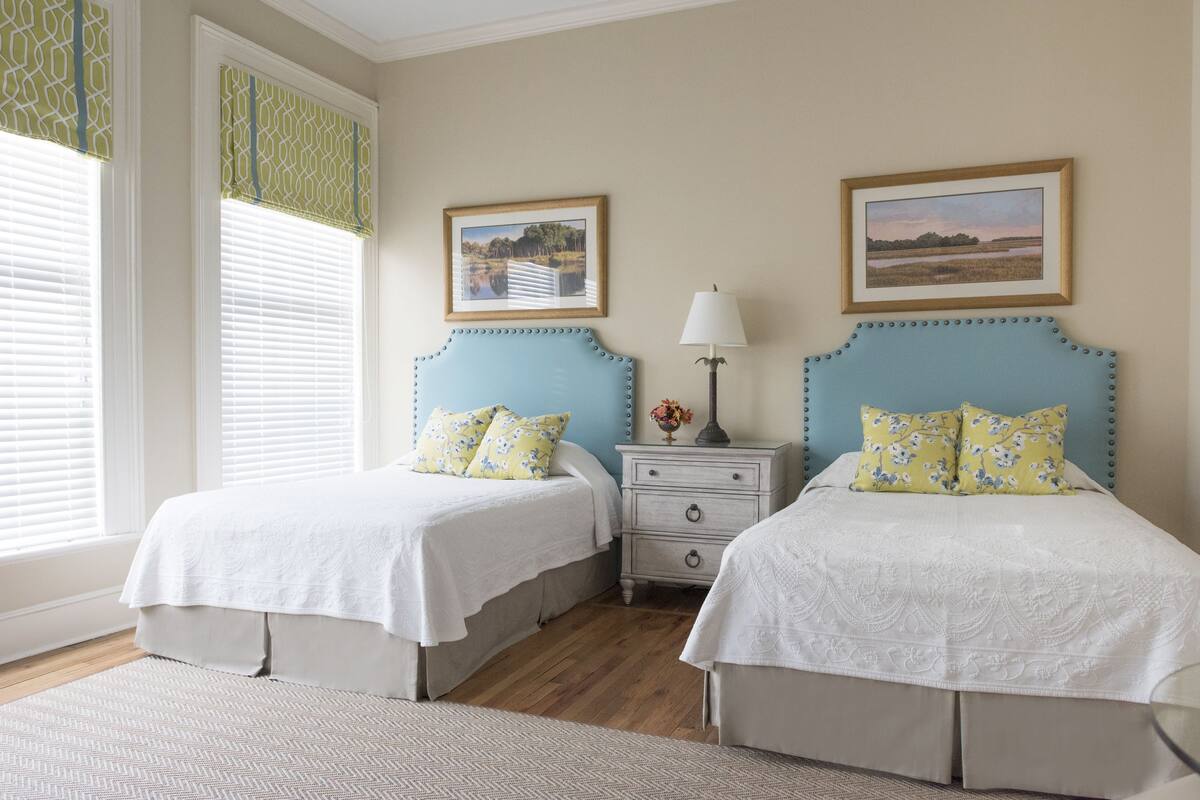 A bedroom with two beds, a nightstand, and two wall-mounted lamps.