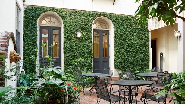 An outdoor patio with brick flooring, metal tables and chairs, and a green ivy-covered wall. - Kings Courtyard Inn (Charleston)