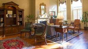 A traditional living room with a fireplace, bookshelves, a chandelier, and a large mirror. - Kings Courtyard Inn (Charleston)