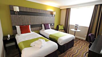 A hotel room with two beds, a desk, a chair, a small table, and a window with curtains.