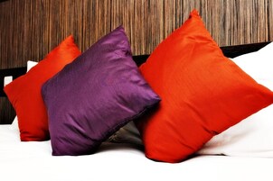 Una cama con tres almohadas en colores rojo, morado y naranja.